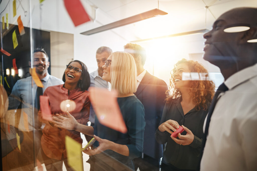 Diverse group of smiling businesspeople brainstorming with sticky notes on a glass wall while working together in a modern office