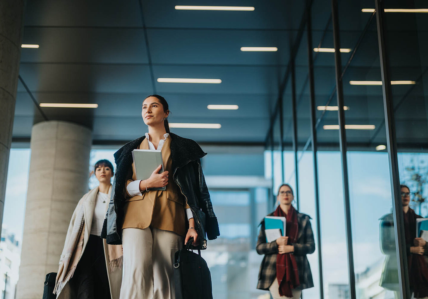 A group of professional women walking confidently through a modern urban area, holding documents and symbolizing collaboration, success, and professionalism in a business-oriented outdoor setting.