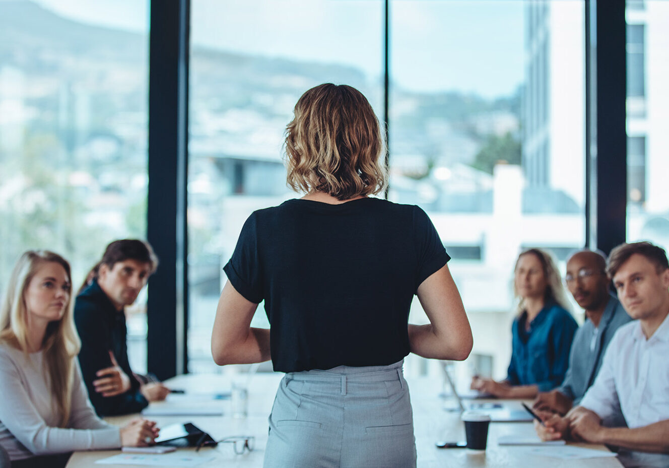 Woman standing up in front of boardroom of colleagues